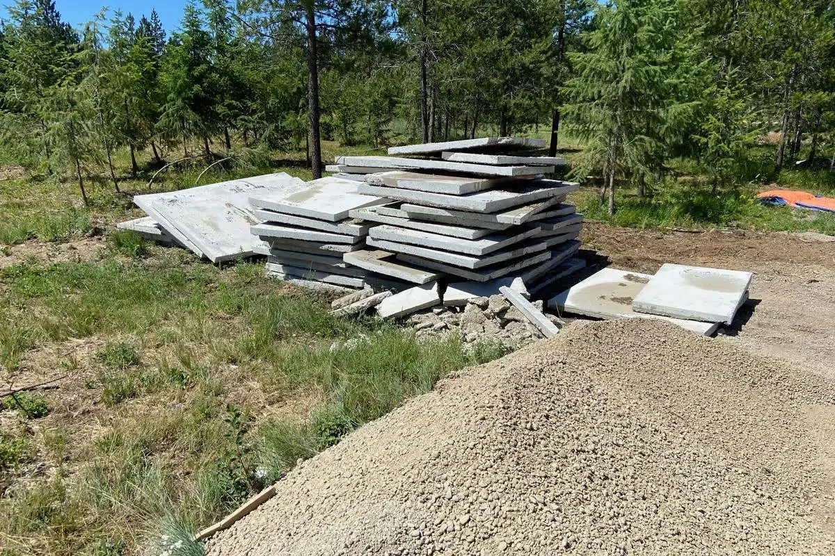 Stack of removed concrete slabs beside a gravel pile at a wooded job site