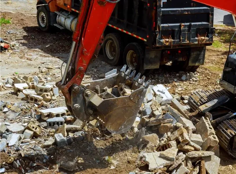Excavator bucket loading broken concrete debris into a dump truck