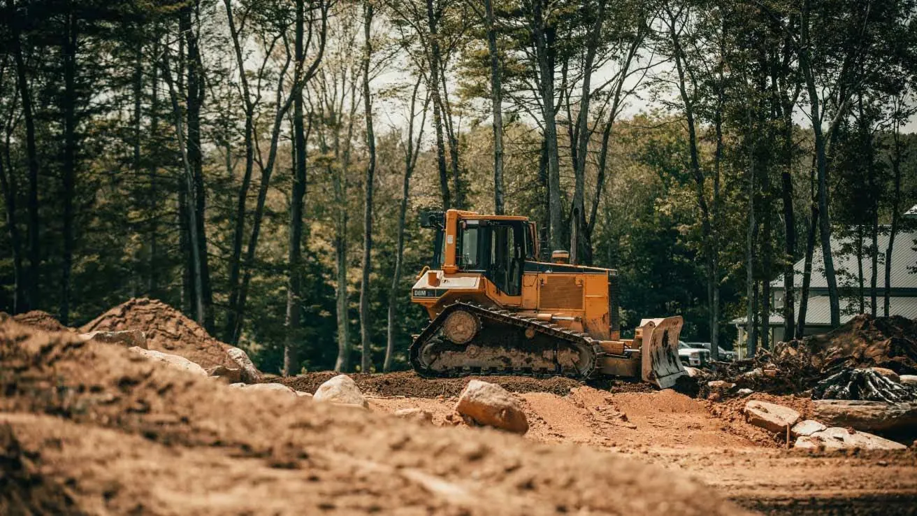 Bulldozer grading a dirt site for construction in a wooded clearing